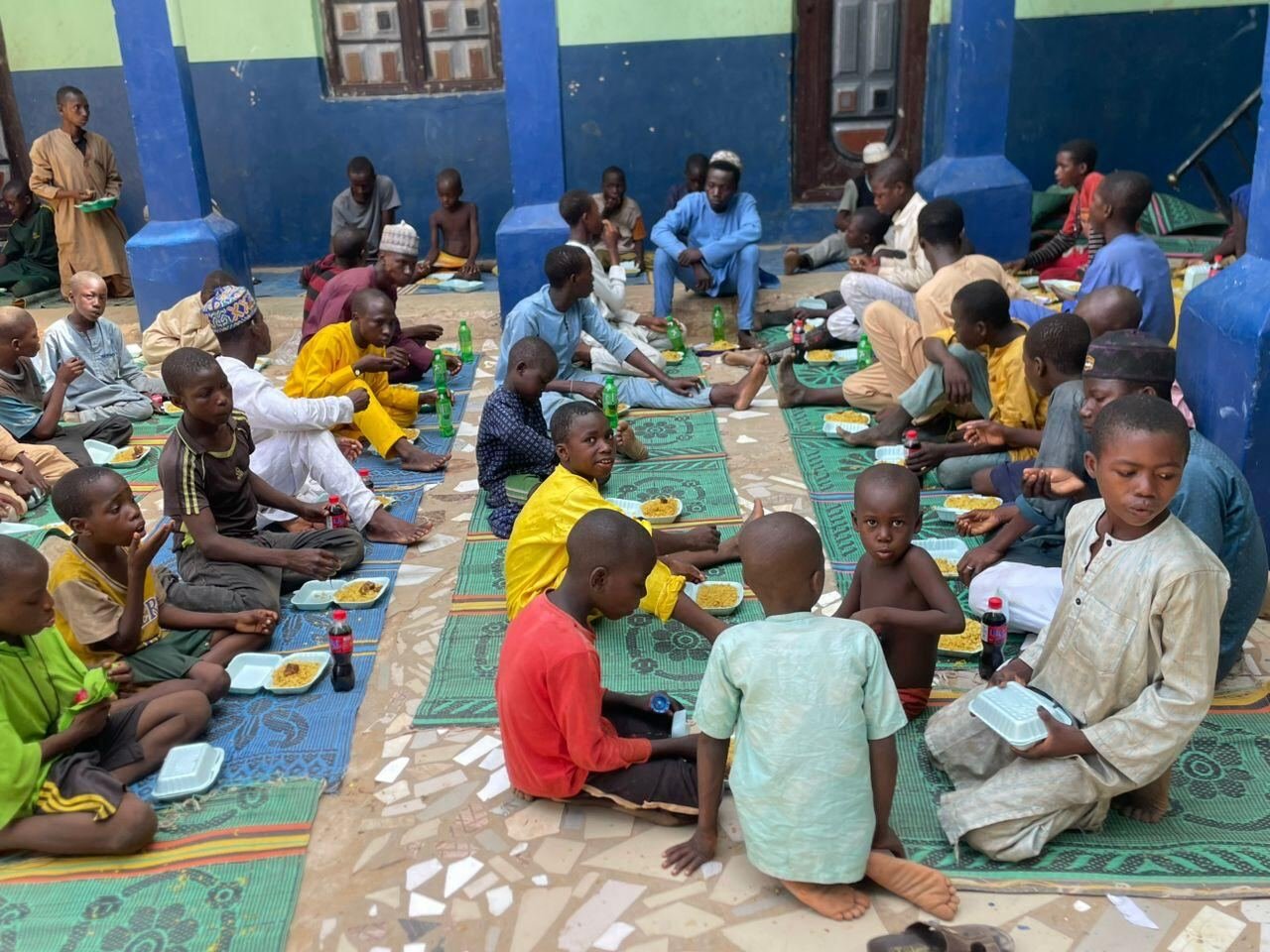 Rows of children sharing a meal in the orphan centre courtyard
