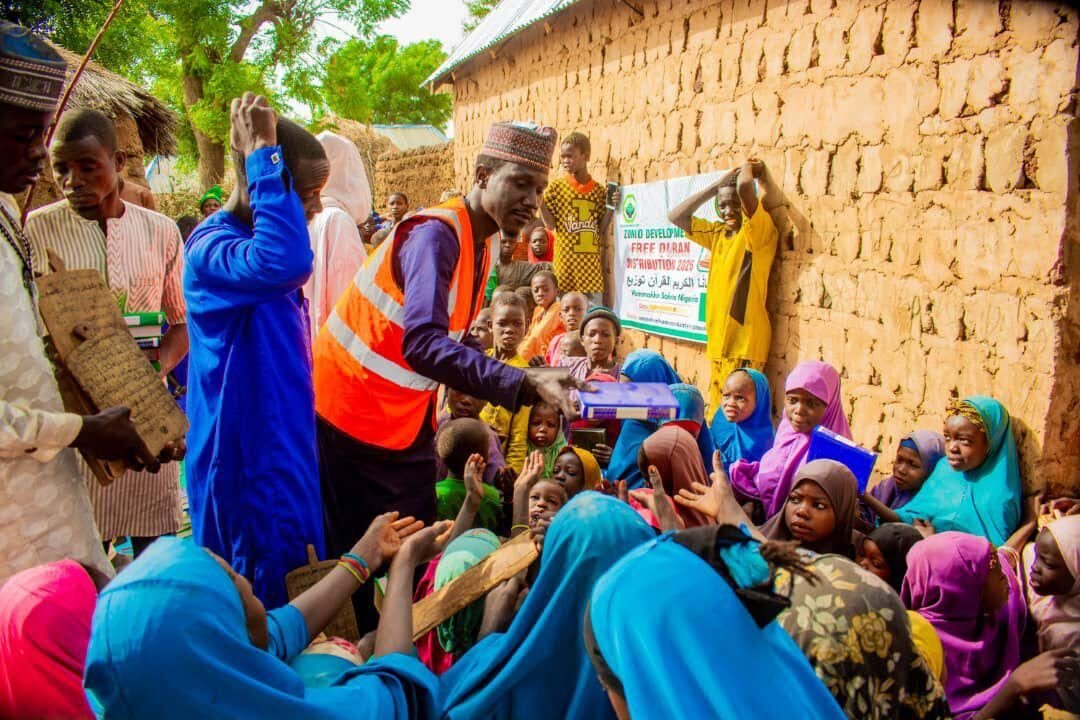 A volunteer giving Qurans to girls by a mud-brick wall